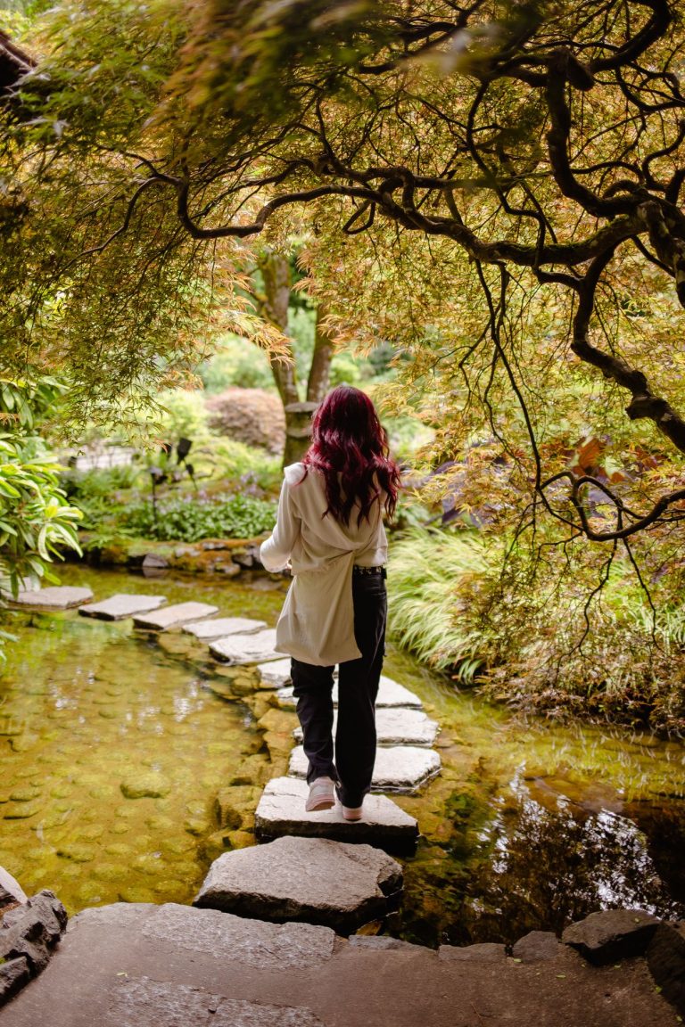Woman walking across stepping stones in a garden, representing small continuous steps forward