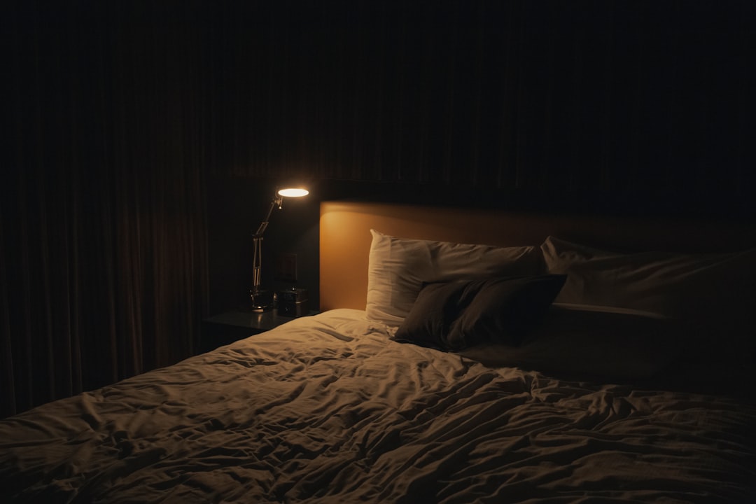 A dim table lamp glowing beside a bed in the evening