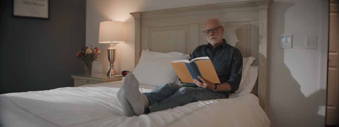 A man reading a book while relaxing in bed with a lamp glowing