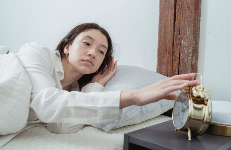 Woman in pajamas turning off an alarm clock in bed