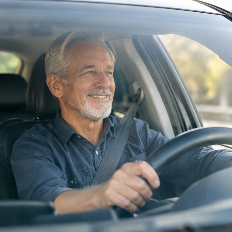Man in his 60s driving a car in daylight with hands relaxed on the steering wheel